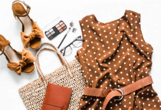 Polka dot summer brown dress, suede wedge sandals, eco straw tote bag, cosmetics on a light background, top view. Women's clothing set